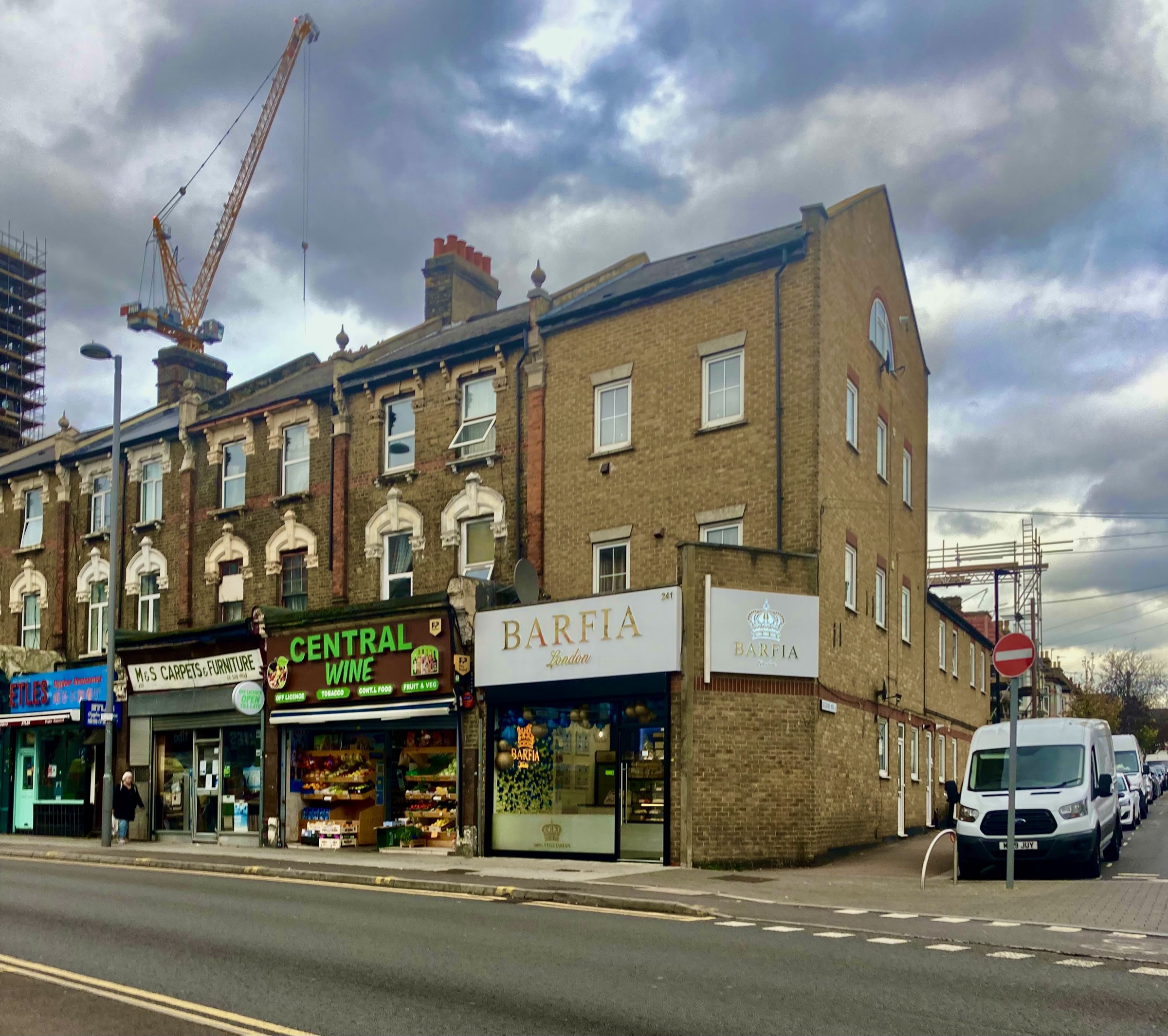 The Central Wine shopfront on Hoe Street, Walthamstow, seen from across the road with its green sign and fruit and veg display.